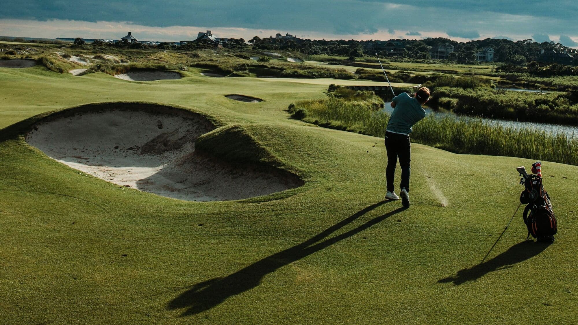 A golfer mid swing on a links fairway under a wide cloudy sky
